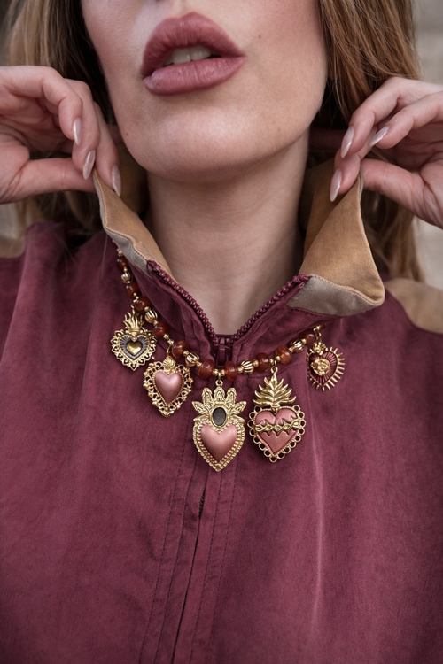Collana con cuori sacri e dettagli smaltati.
Un gioiello ricco di simbolismo e carattere, che unisce il fascino dei cuori sacri a tonalità calde e avvolgenti. Le perline aranciate si alternano a dettagli dorati e pendenti smaltati, creando un mix vibrante e super distintivo